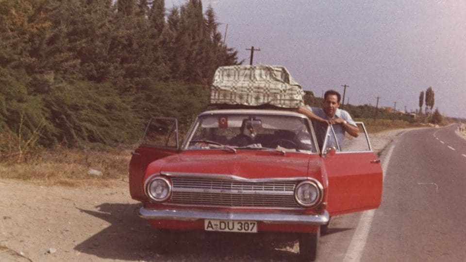 Ein altes Foto mit einem rotem Auto und Gepäck auf dem Dach