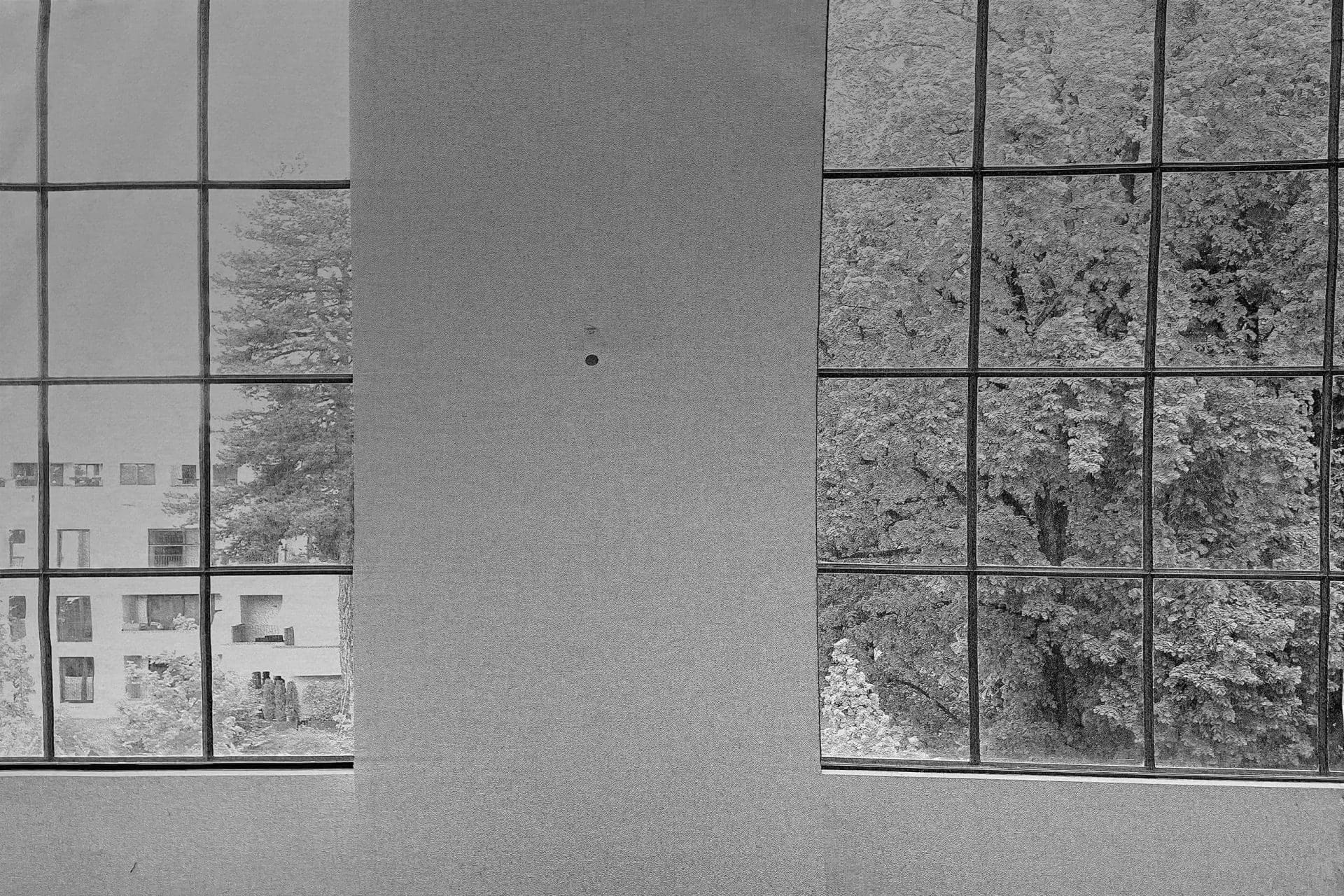 Ein reduziertes schwarz-weiß Foto von einem einfarbigen Stoff der vor einer Fensterfront verläuft